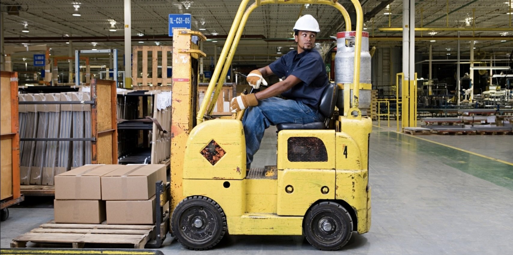 man looking backwards driving a yellow forklift in a warehouse